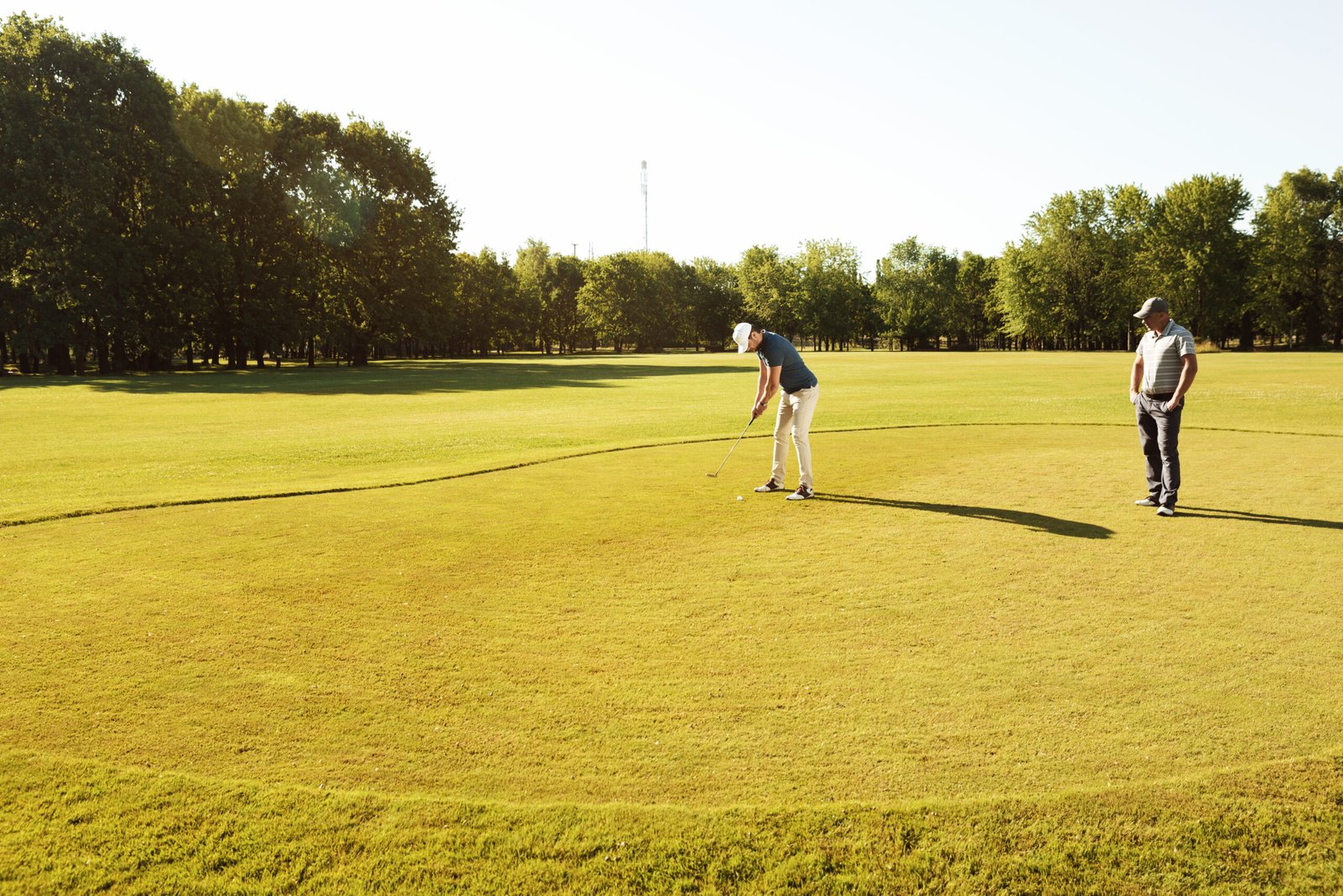 Young sportsman practicing golf with his teacher while standing on a green course
